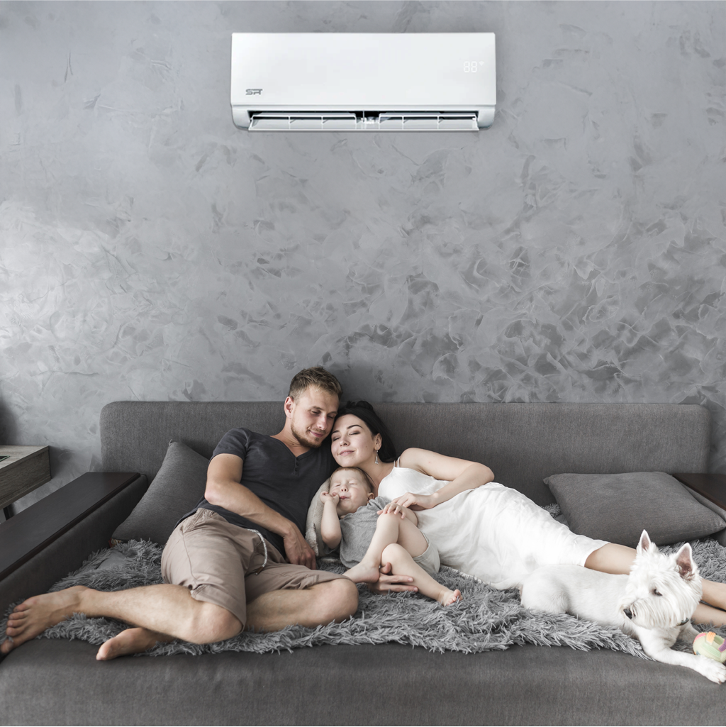 A man and woman relax on a couch with their baby, enjoying the comfort of an air-conditioned room